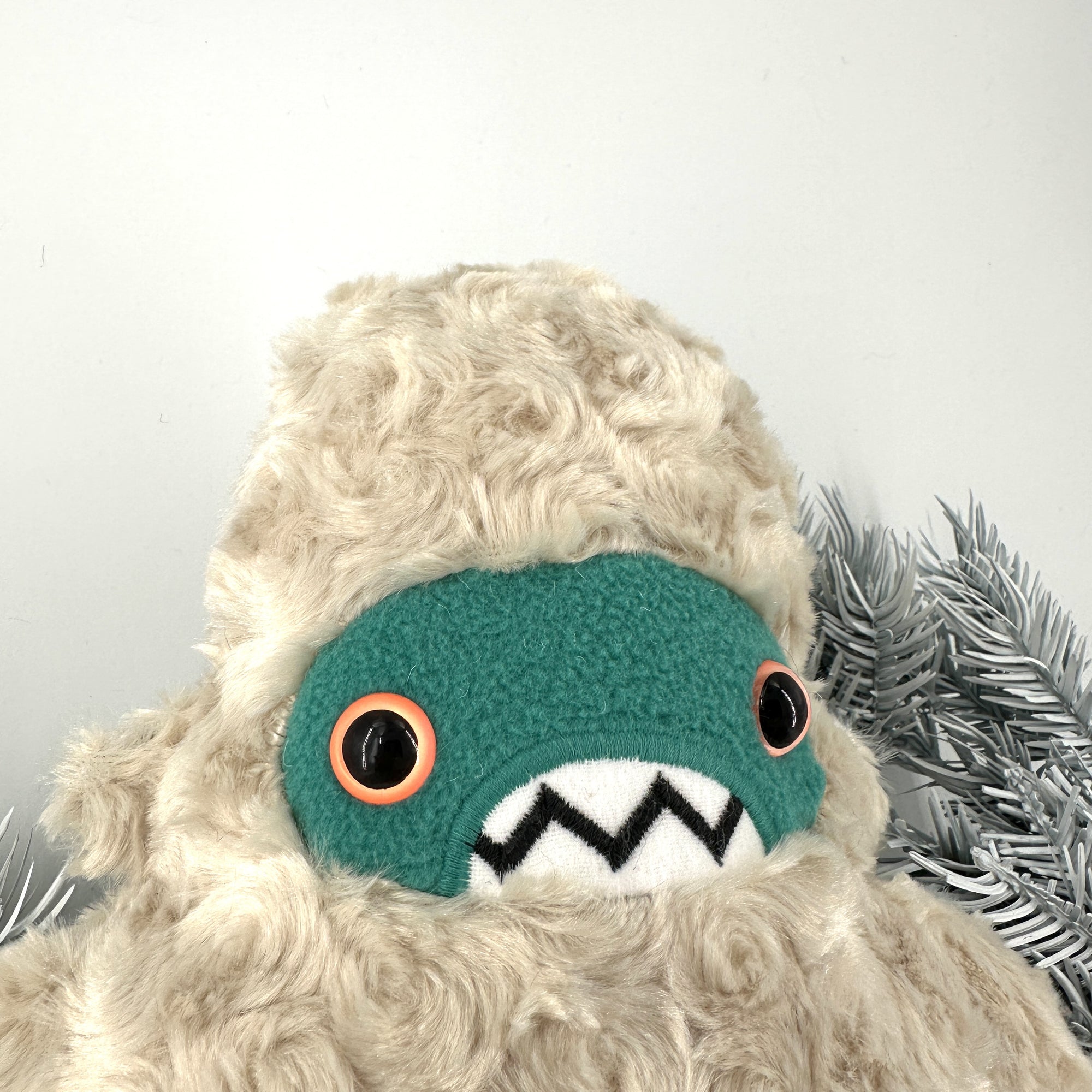 Close up of a furry creature with cream colored, curly texture. It has a teal face, big orange eyes, and toothy grin . Textures white background.