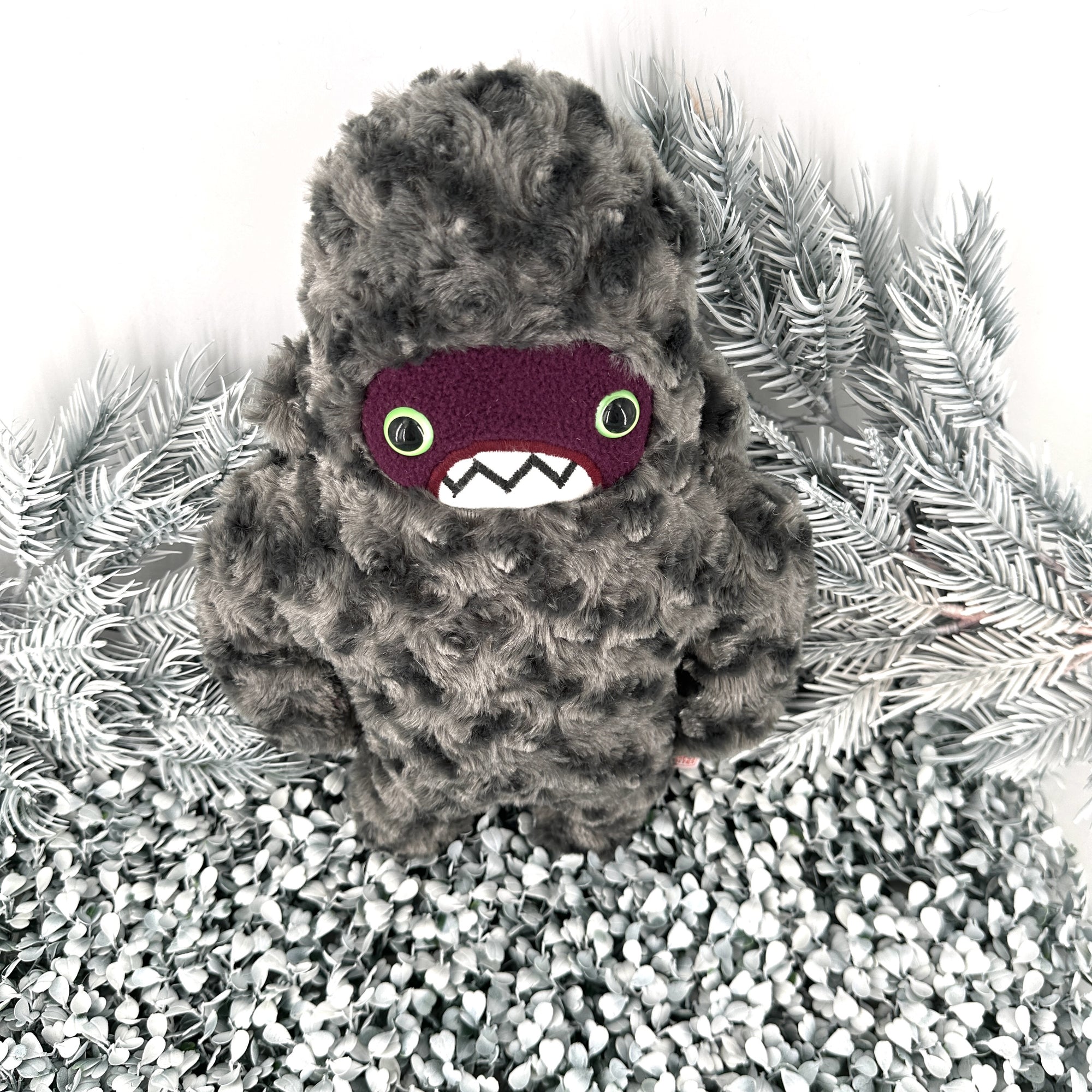 A furry creature boasts a gray, curly texture. It has a dark purple face, big green eyes, and toothy grin . Textures white background.