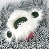 A plush toy resembling a white yeti with a fluffy faux fur head, dark face, and expressive eyes lies on a textured, pebble-like surface. A tiny bit of red fur is visible on the underside.