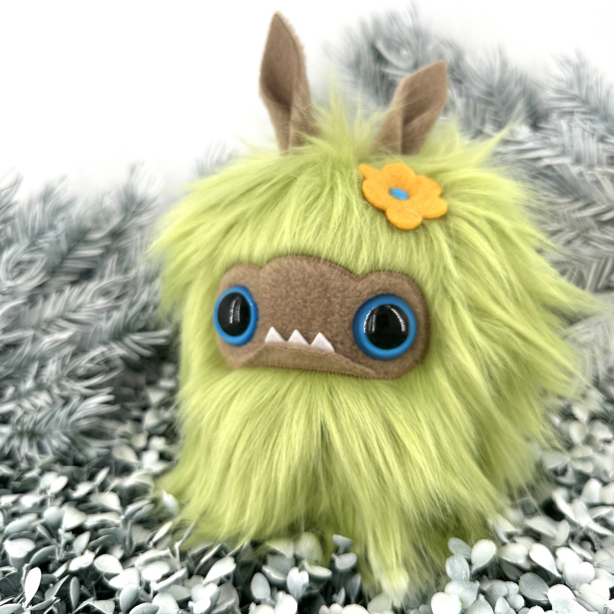 Bright green faux fur creature with big blue eyes and underbite sits on white foliage.