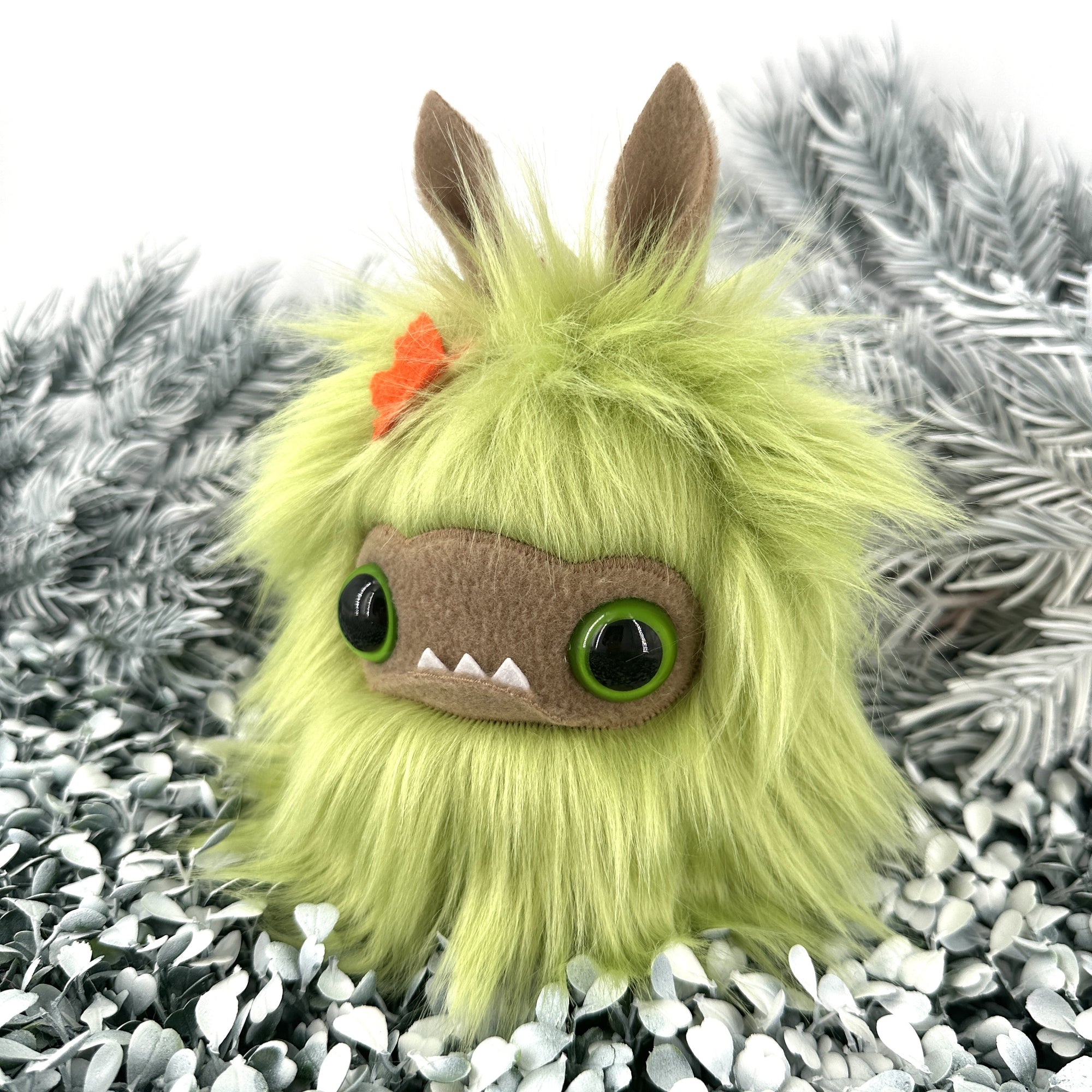 Bright green faux fur creature with big green eyes and underbite sits on white foliage.