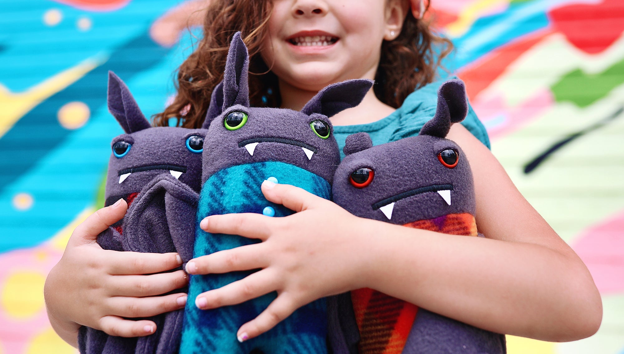 Close up of girl holding 3 plush pajama bats with colorful painted backdrop.