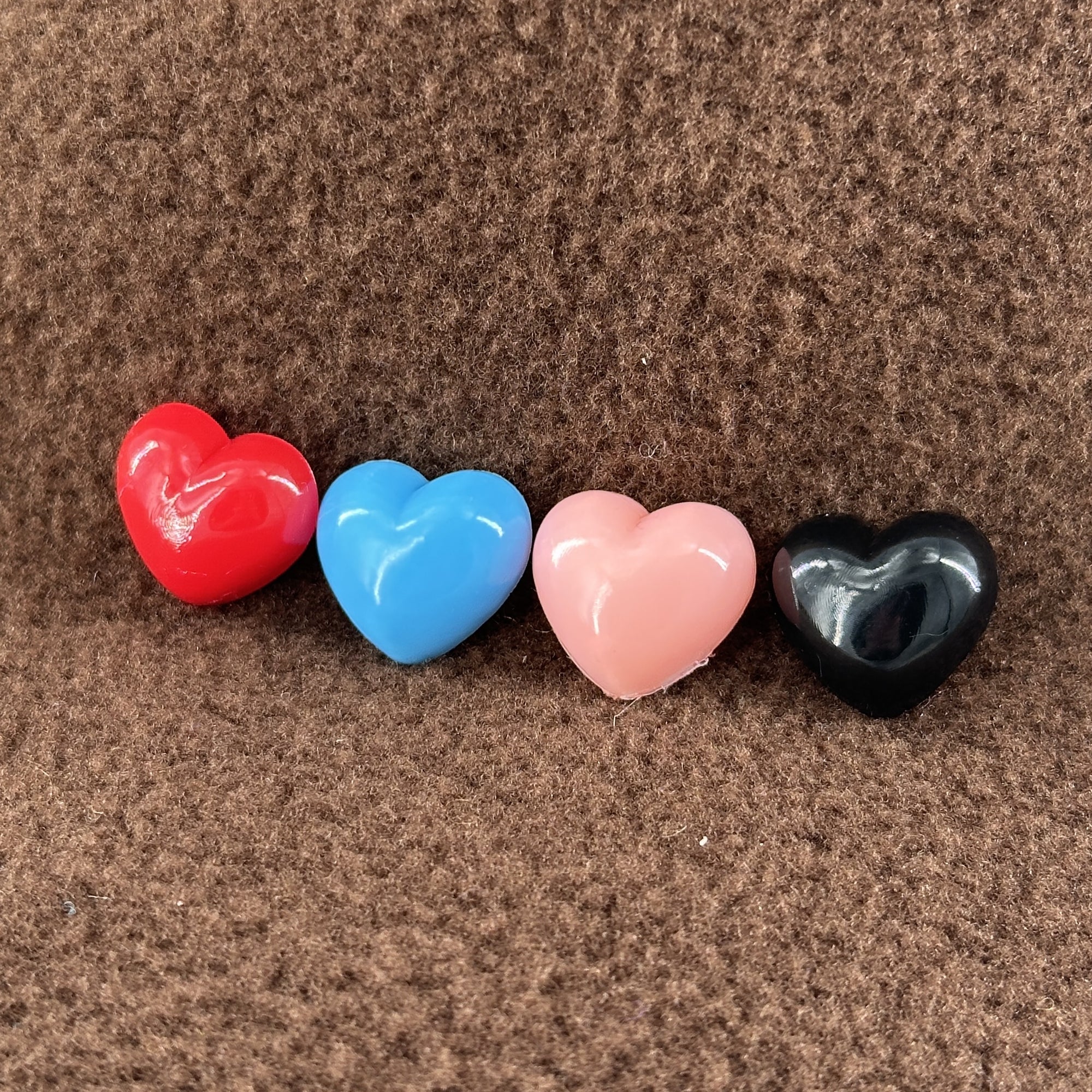 A row of four different colored plastic hearts sit atop of a brown fleece background.