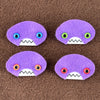 Four oval shaped purple faces with different eye colors and pointed teeth sit atop a brown fleece background.