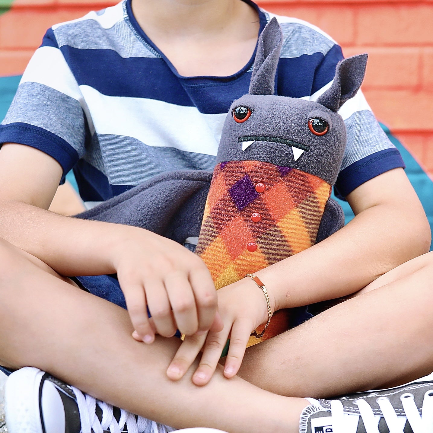 Boy sits crosslegged while holding a plush pajama bat stuffed animal.