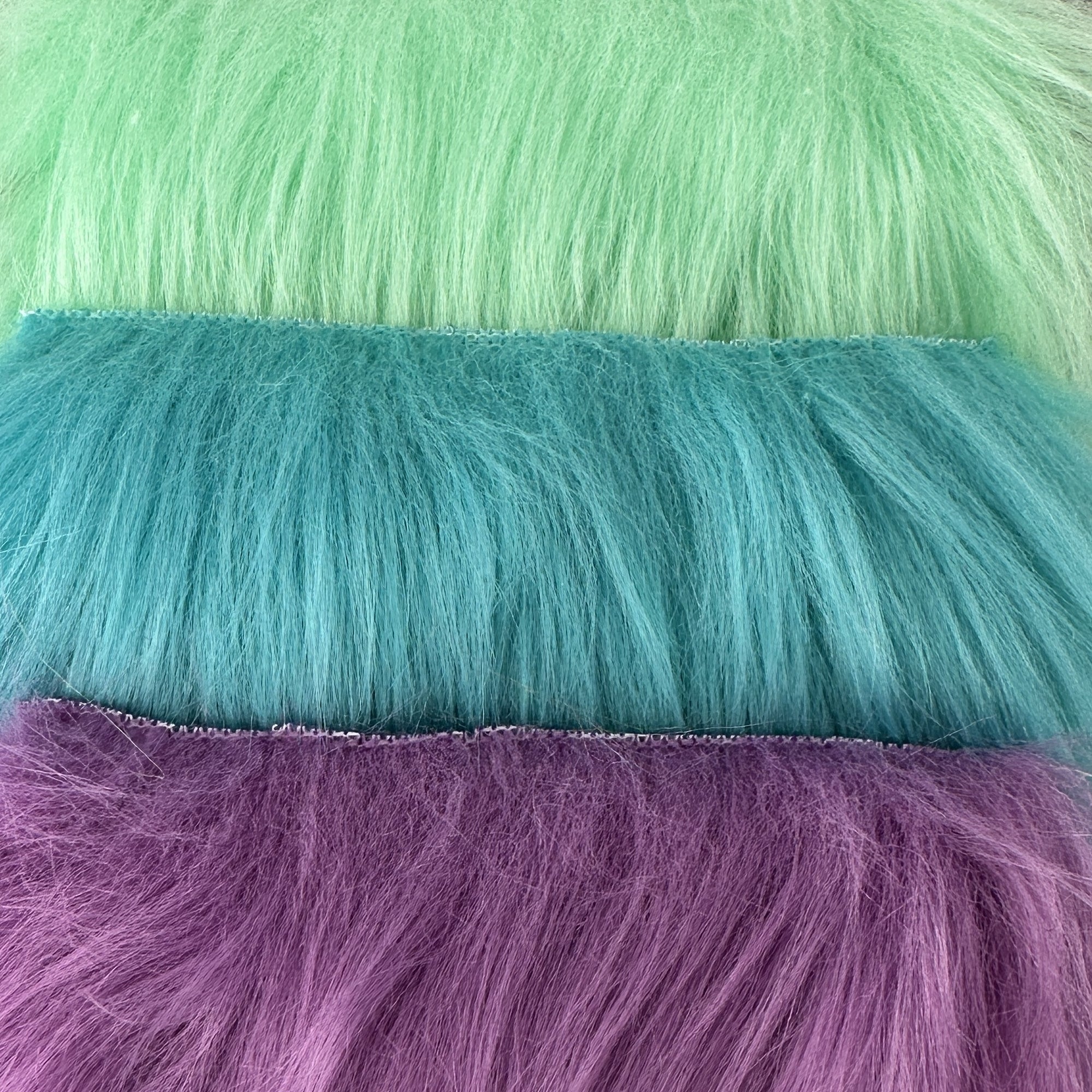 An  closeup array of faux fur in cool shades of mint green, teal blue, and lavender purple.