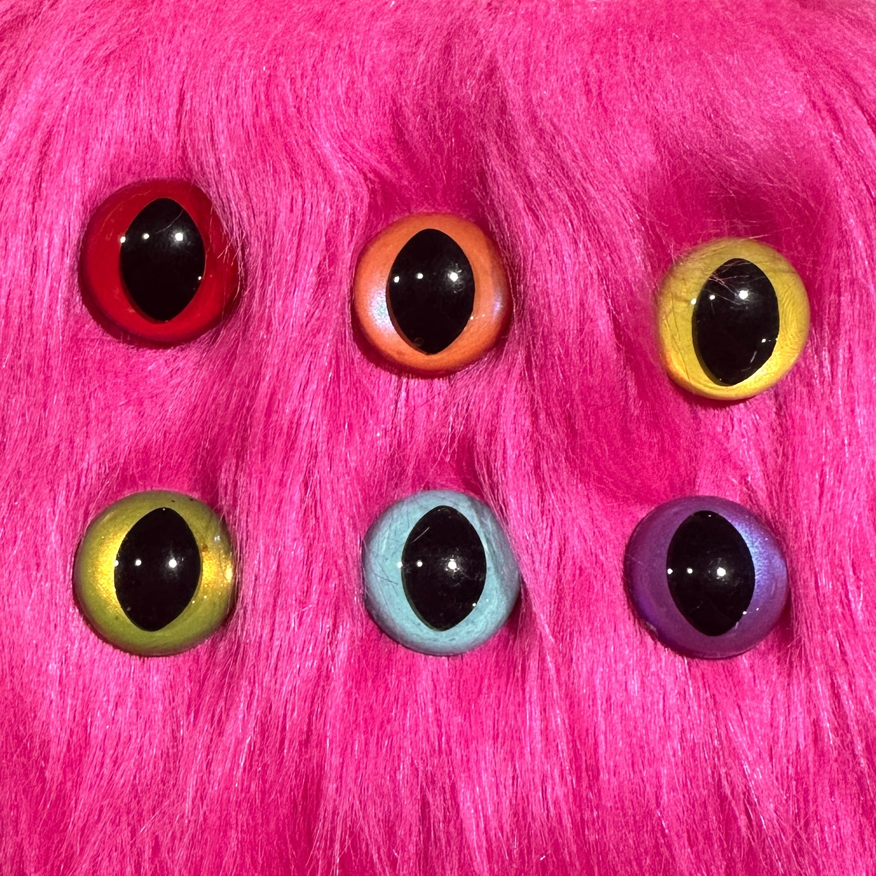 Slit pupil safety eyes in six colors lay atop pink faux fur.