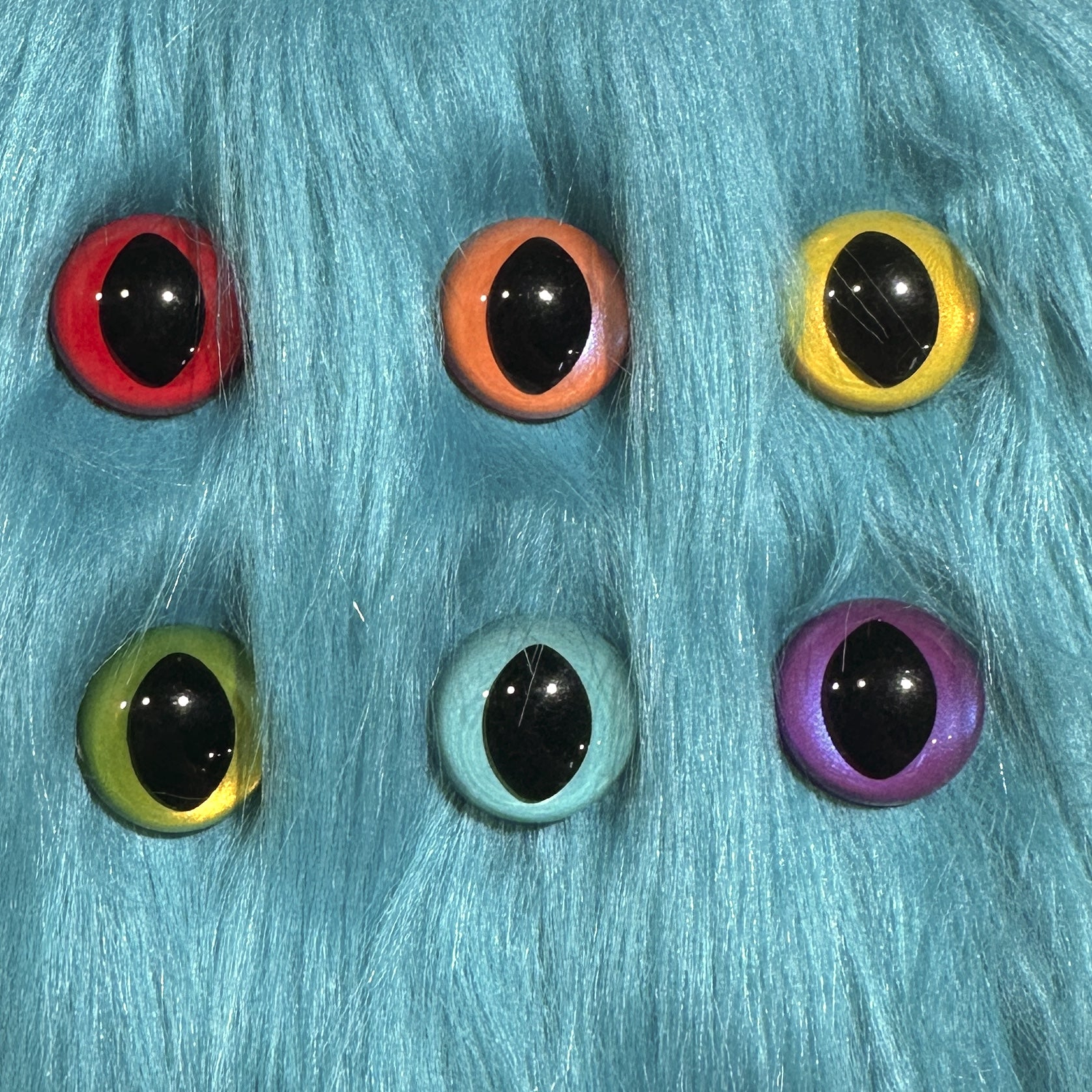 Slit pupil safety eyes in six colors lay atop teal faux fur.