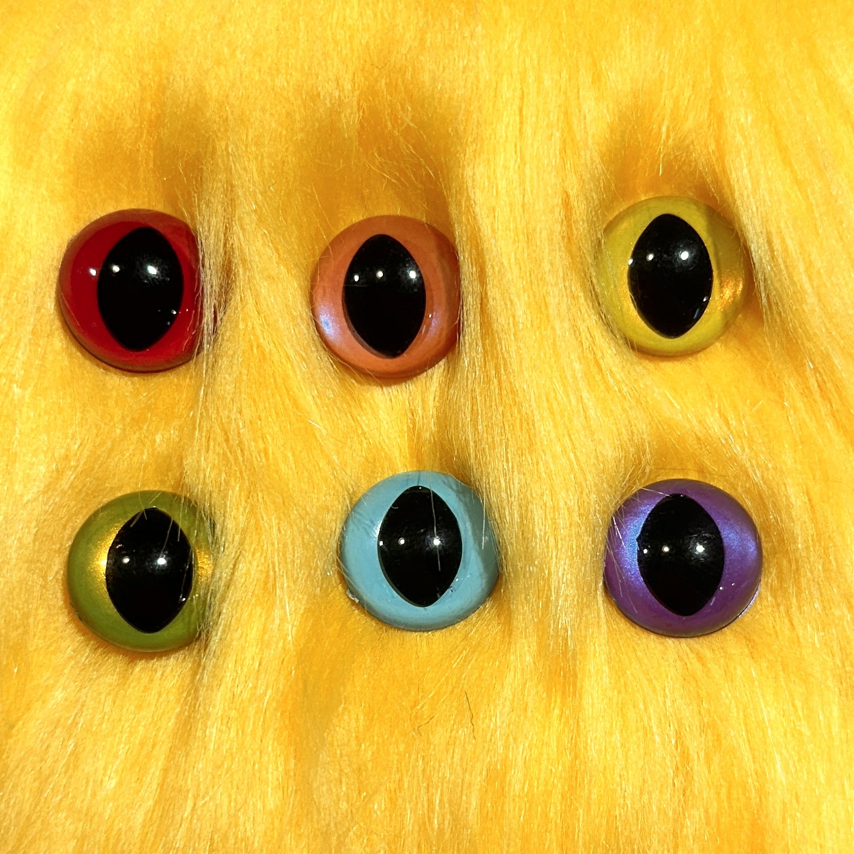 Slit pupil safety eyes in six colors lay atop yellow faux fur.