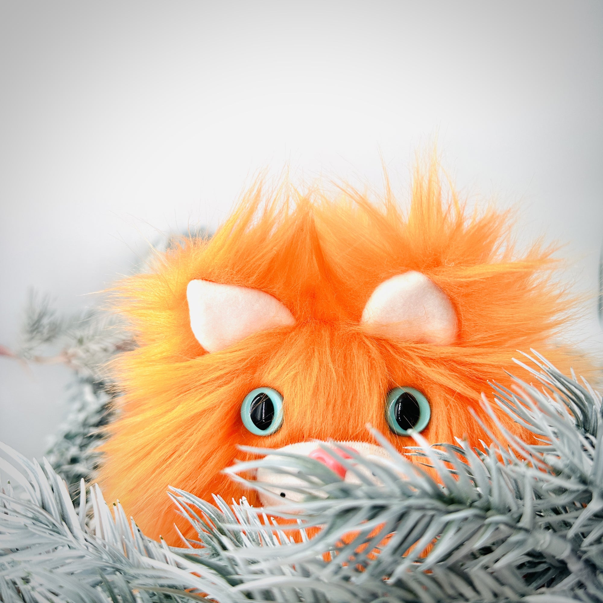 Orange cat stuffed animal with light blue eyes half hidden by white boughs.