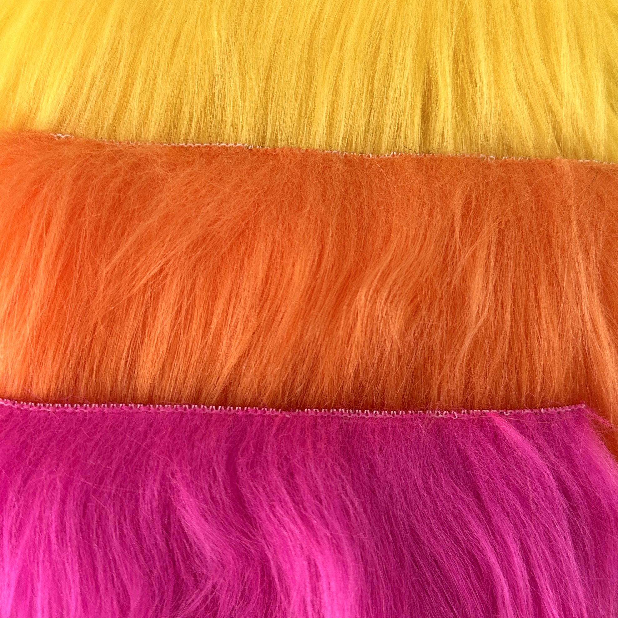 An  closeup array of faux fur in warm tones of yellow, orange, and hot pink.