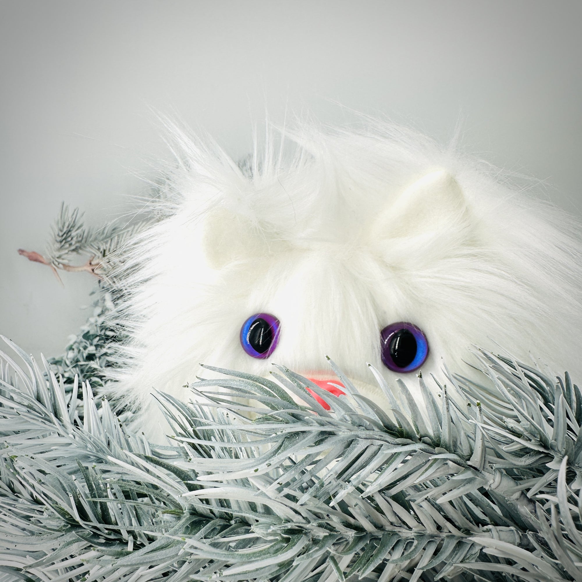 A white catball plush peeks out from behind a white bough.