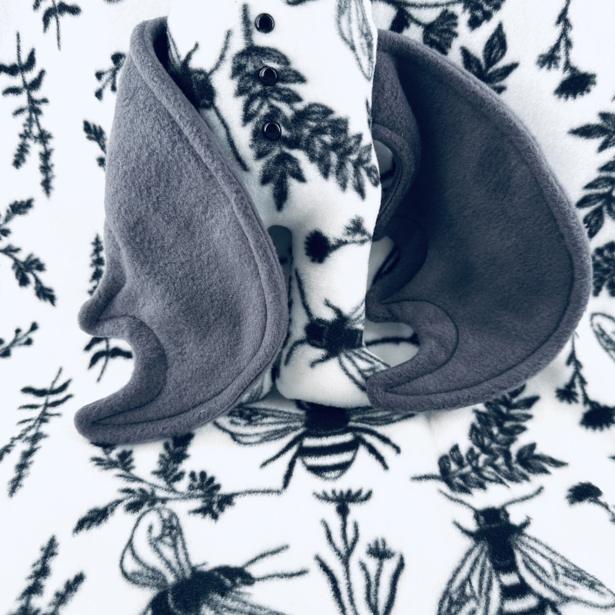 A plush bat wearing white floral pajamas sits a top a background of the same patterned fleece.