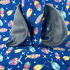 A plush bat wearing blue fleece with bug pattern pajamas sits a top a background of the same fleece.