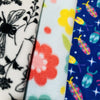 Three fleece fabric patterns are shown: one with black floral designs on white, another with colorful large flowers on a light background, and the last featuring  bright insect and star motifs on a blue backdrop.