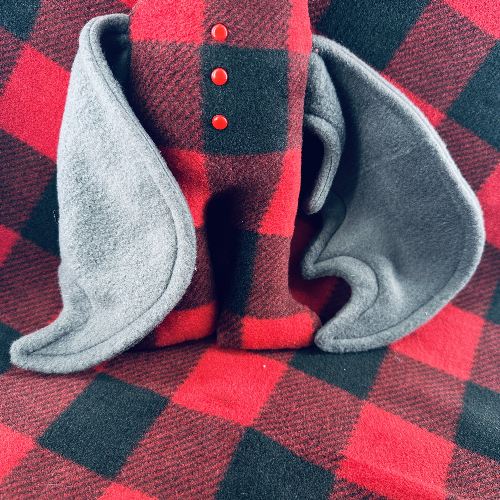 A plush bat wearing red plaid pajamas sits a top a background of the same plaid fleece.