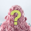 A plush figure, part of the Custom Woolly Yeti collection, is sheathed in fluffy pink fabric with its back turned. A large yellow question mark is superimposed on it, adding an air of mystery. The background remains a light gray backdrop.