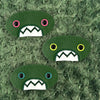 Three plush, green, oval-shaped patches with jagged mouths and colorful eyes are set against a textured, sage background resembling fur.