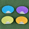 Four oval shaped faces in different colors and pointed teeth sit atop a green fleece background.