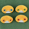 Four oval shaped orange faces with different eye colors and pointed teeth sit atop a green fleece background.