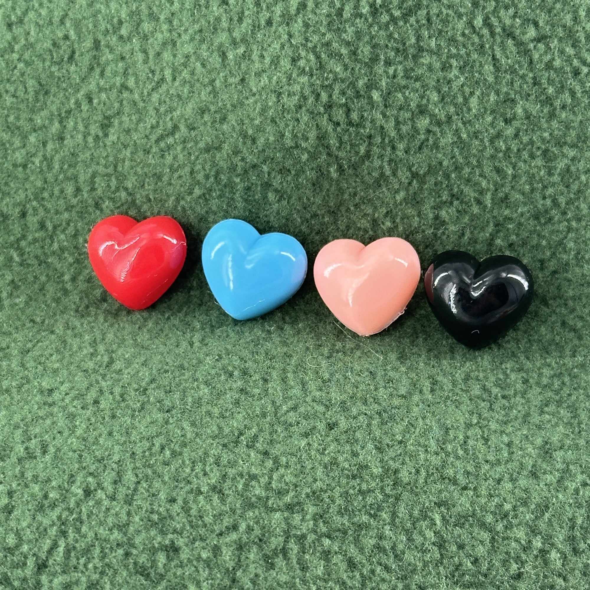 A row of four plastic hearts in different colors sit atop a green fleece background.