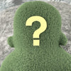 A small green fleece figure with a question mark where its face should be with blurred white background.