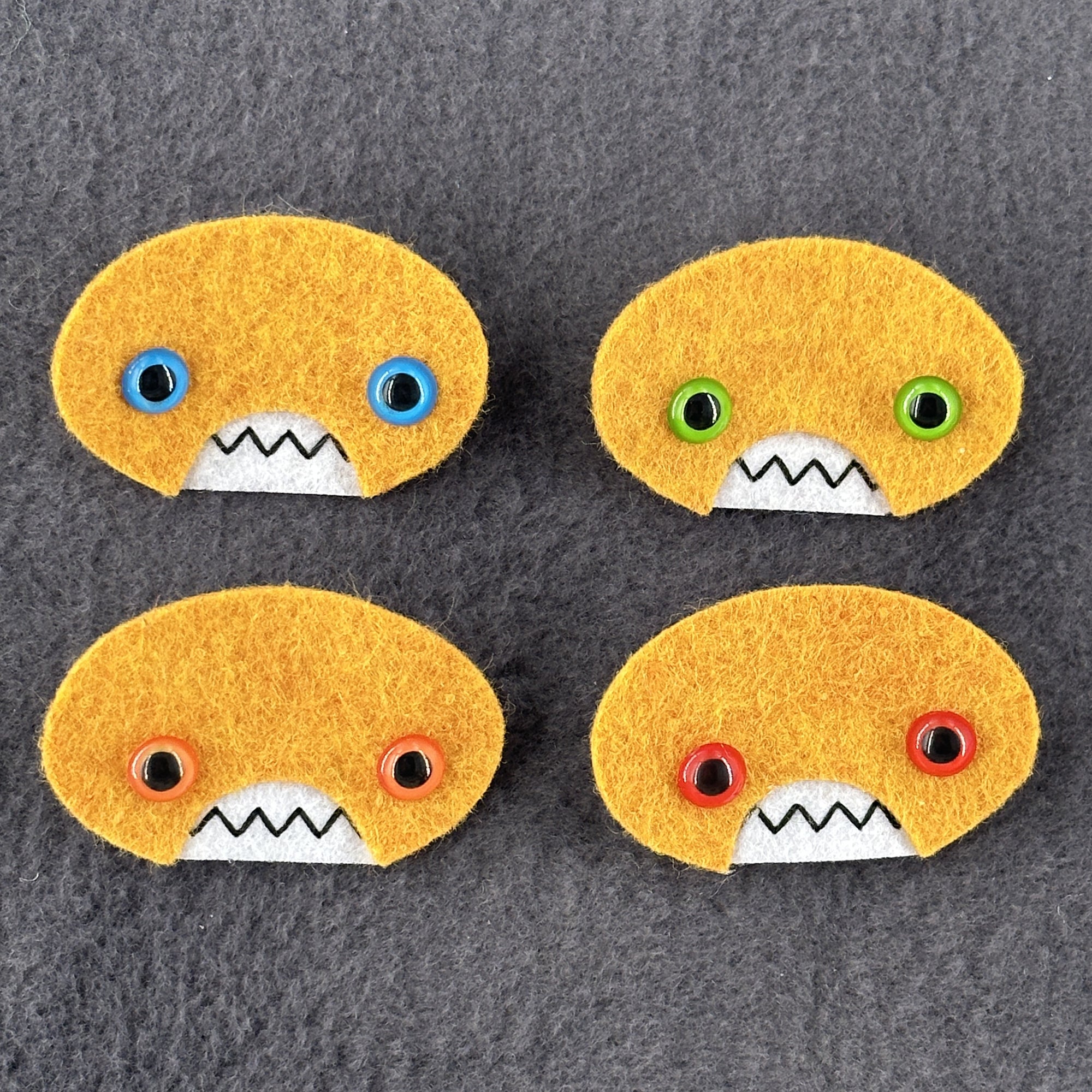 Four oval shaped orange faces with different eye colors and pointed teeth sit atop a grey  fleece background.