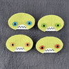 Four oval shaped green faces with different eye colors and pointed teeth sit atop a grey  fleece background.