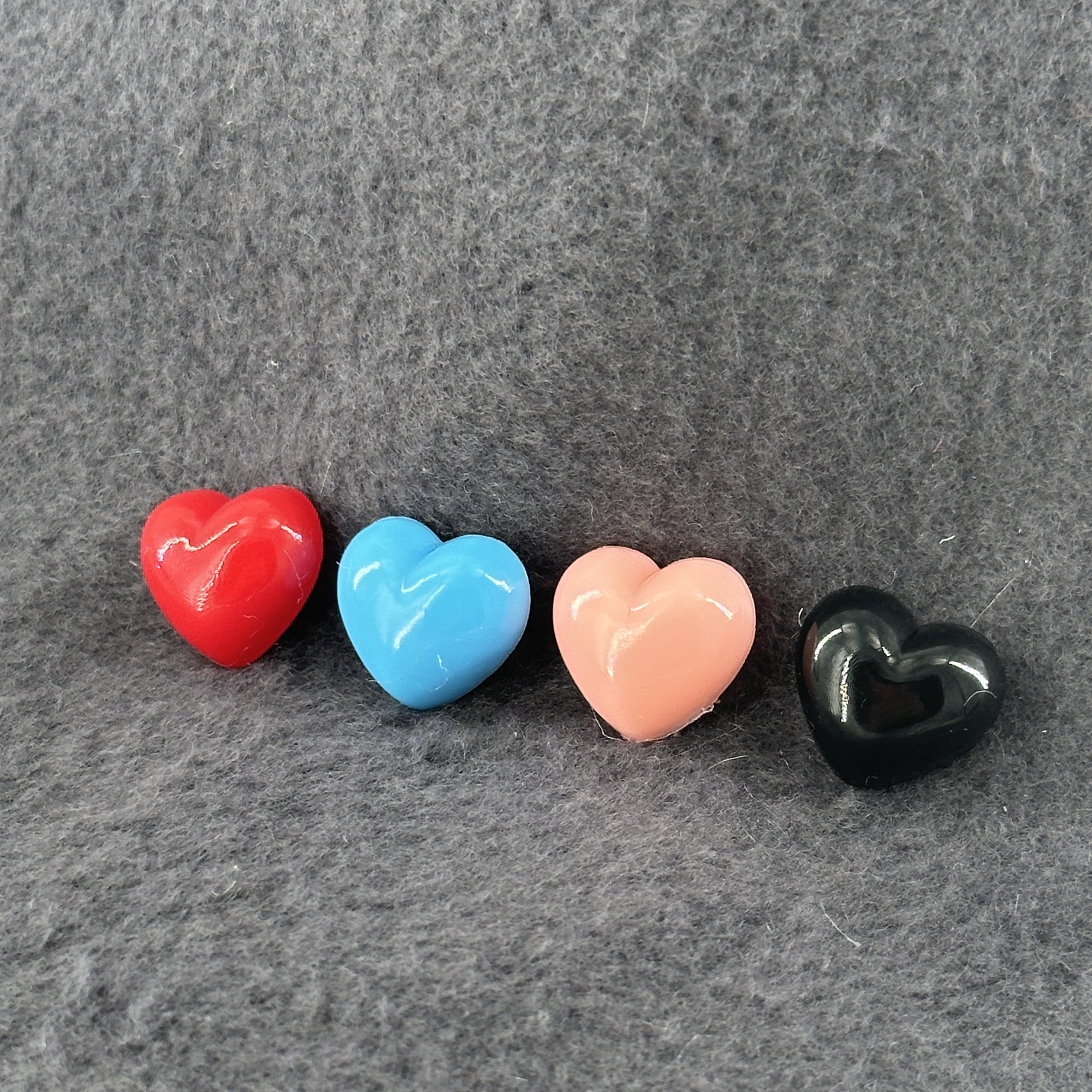 A row of four plastic hearts in different colors sit atop a sand colored fleece background.