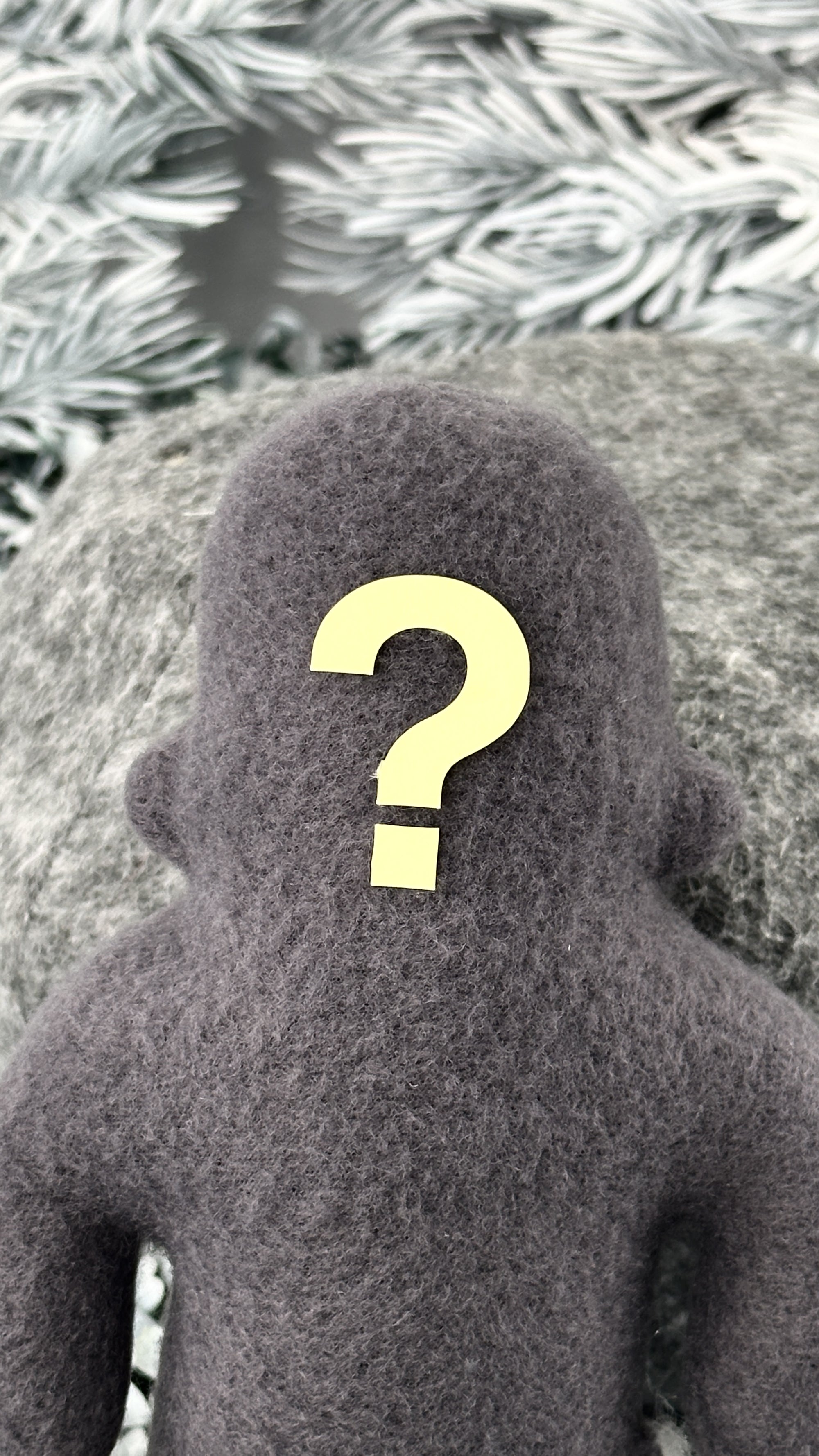 A small grey fleece figure with a question mark where his face should be stands in front of a textured grey background.