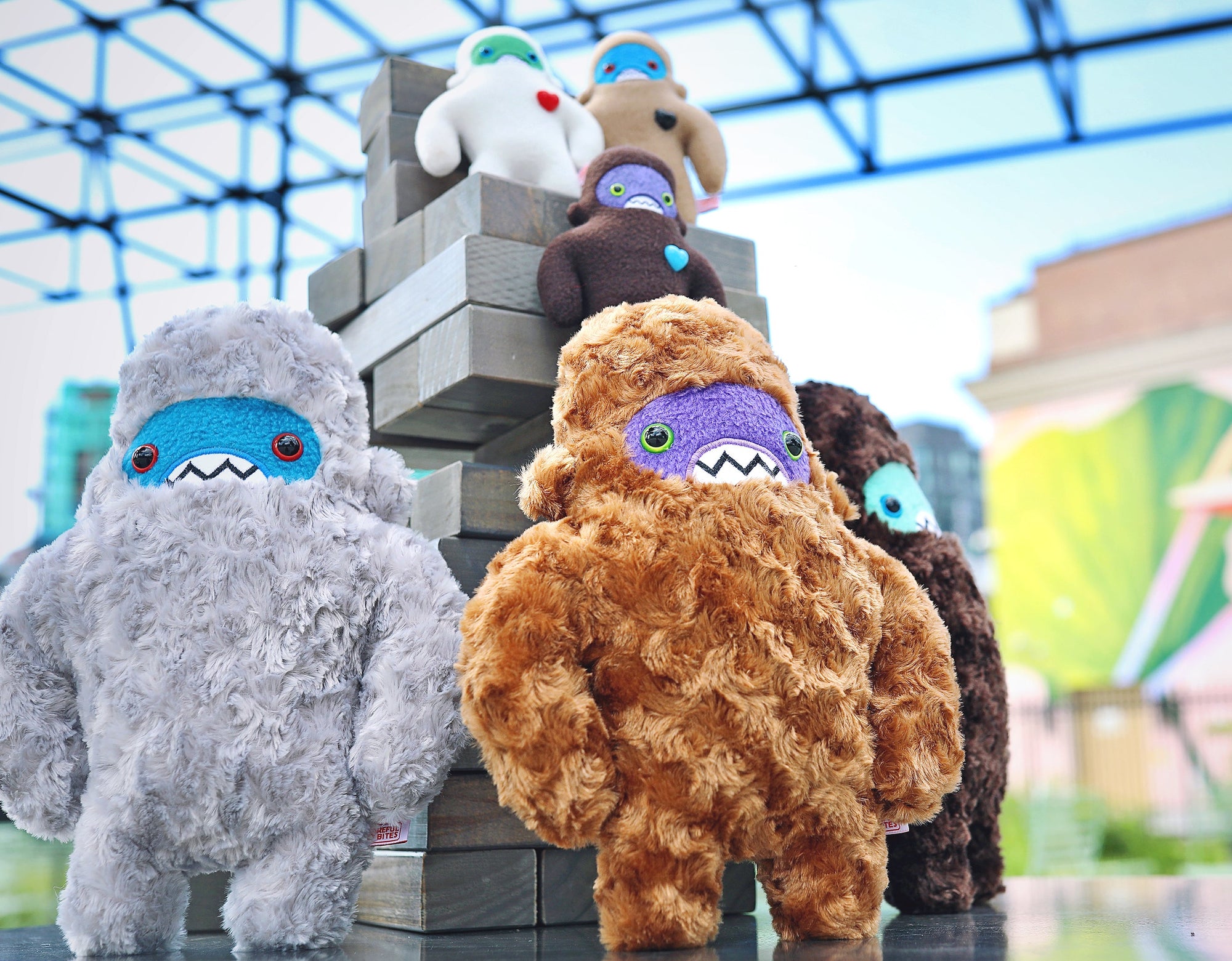 A group of six sasquatch plush, three large and three small, sit atop a large jenga block pile looking adorable.