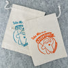 Two drawstring bags with "take me on an adventure" and a sasquatch illustration. One bag is in blue ink the other is orange.