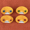 Four oval shaped orange faces with different eye colors and pointed teeth sit atop an orange fleece background.