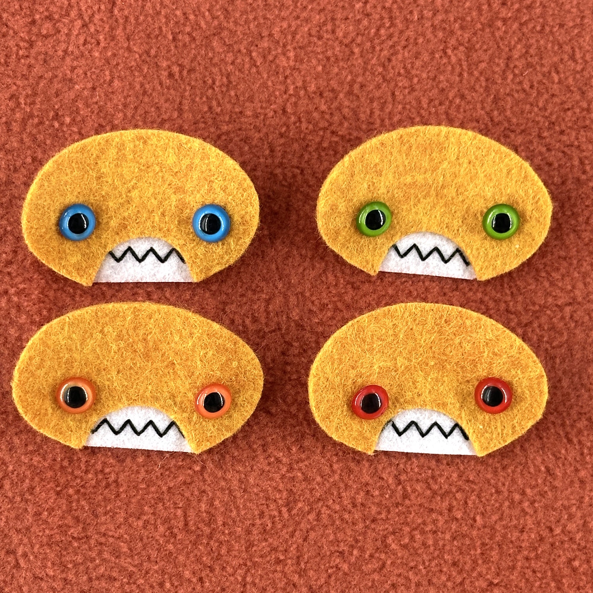 Four oval shaped orange faces with different eye colors and pointed teeth sit atop an orange fleece background.