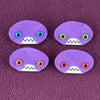 Four oval shaped purple faces with different eye colors and pointed teeth sit atop a purple fleece background.