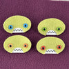 Four oval shaped green faces with different eye colors and pointed teeth sit atop a purple fleece background.