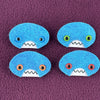 Four oval shaped teal faces with different eye colors and pointed teeth sit atop a purple fleece background.