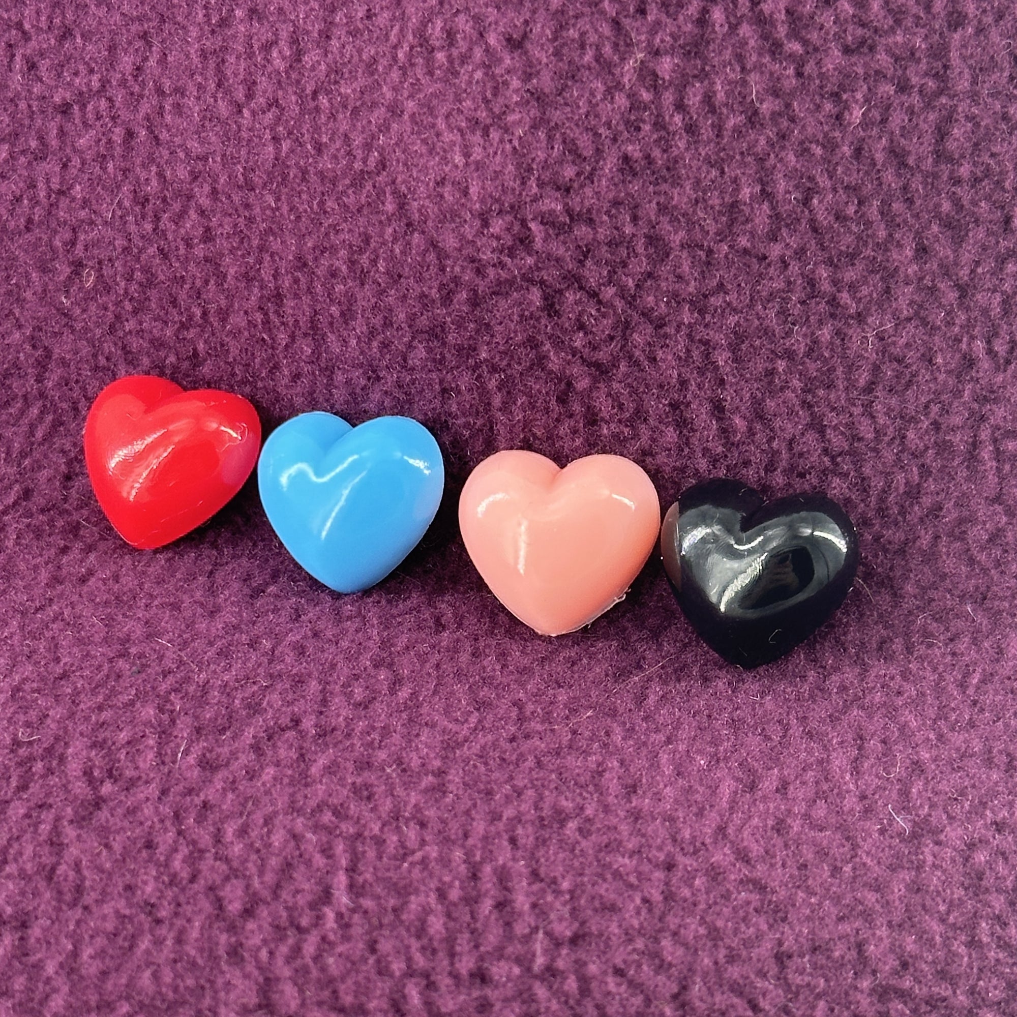 A row of four different colored plastic heart sit atop a purple fleece background.