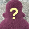 A small purple fleece figure with a question mark face stands in front of white foliage.