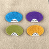 A group of four oval felt faces in different colors sit on top of a sand colored background.