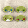 Four oval shaped green faces with different eye colors and pointed teeth sit atop a sand colored fleece background.