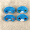 Four oval shaped teal faces with different eye colors and pointed teeth sit atop a sand colored fleece background.