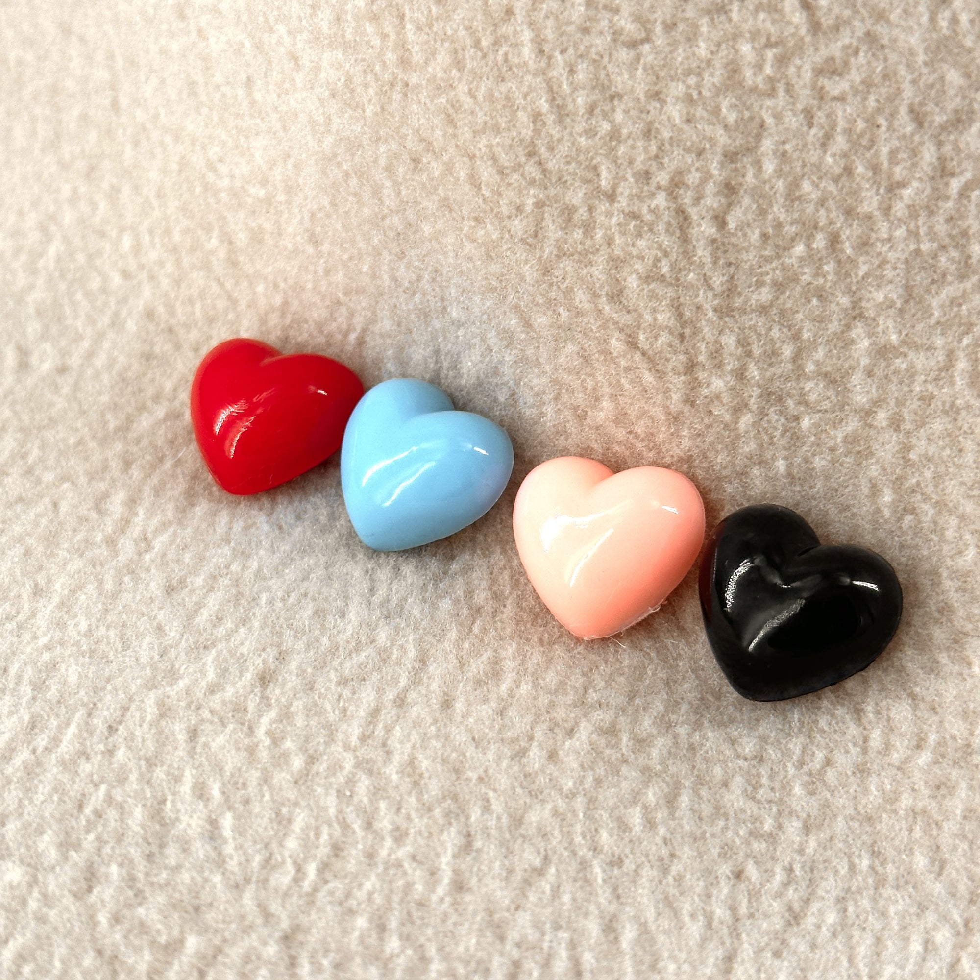 A row of four plastic hearts in different colors sit atop a sand colored fleece background.