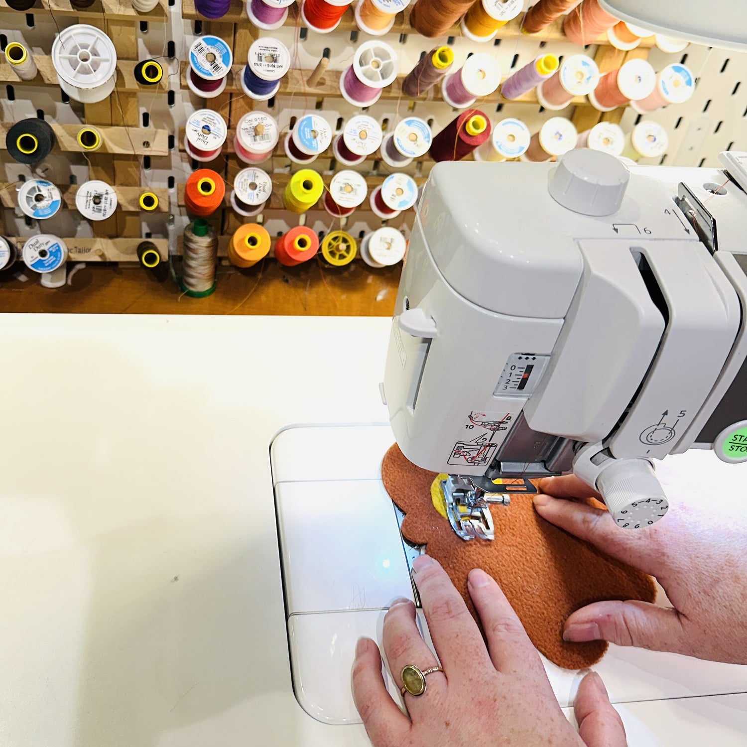 Hands shown using a sewing machine with colorful thread in the background.