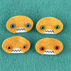 Four oval shaped orange faces with different eye colors and pointed teeth sit atop a teal fleece background.