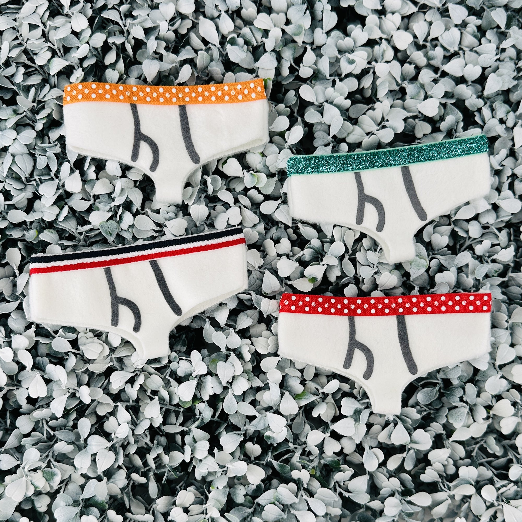 Four pair of various band colors of tiny underwear sit on top of a textured white background.