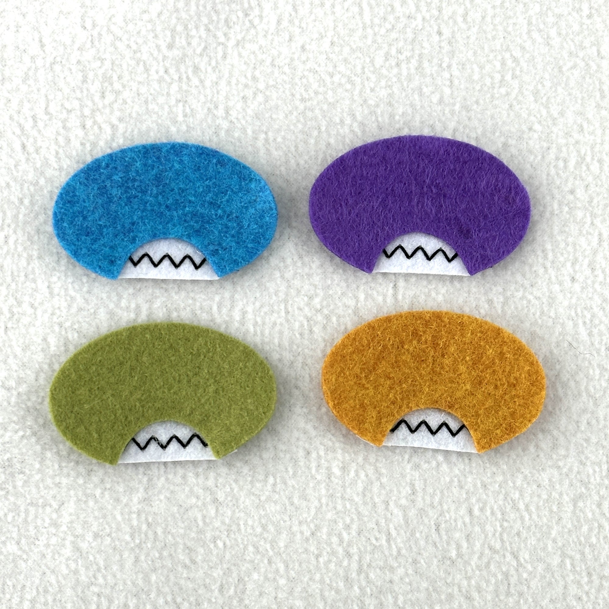 Four oval shaped faces in different colors and pointed teeth sit atop a white fleece background.