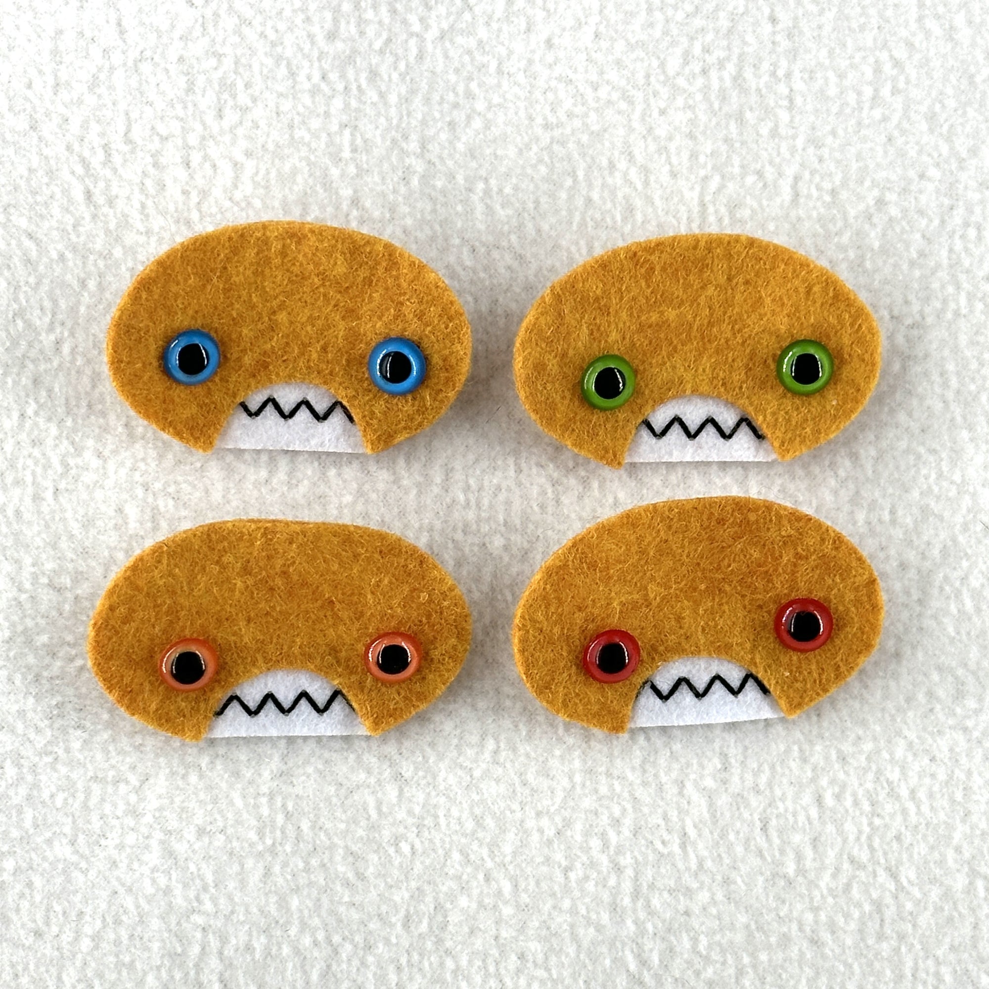 Four oval shaped orange faces with different eye colors and pointed teeth sit atop a white fleece background.