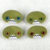 Four oval shaped green faces with different eye colors and pointed teeth sit atop a white fleece background.